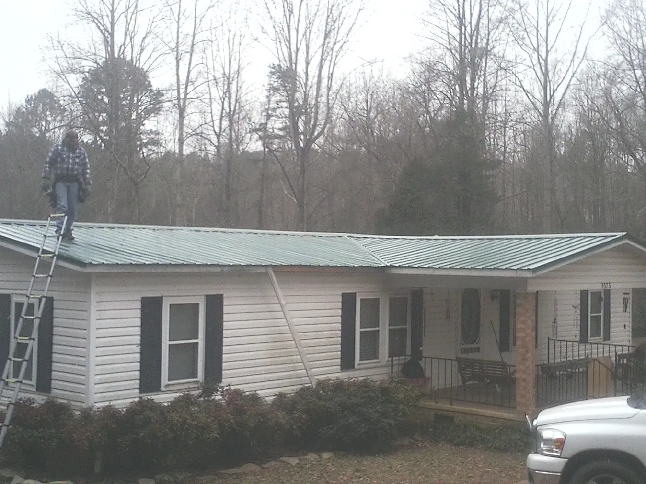 Worker on a ladder beside a new green metal roof on a ranch home in Mattoon
