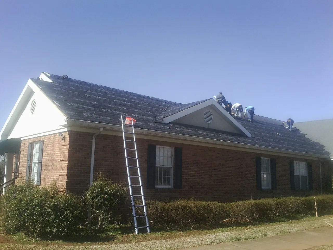 Crew tearing shingles off a brick ranch roof with a ladder set — Emergency Roof Repair work by our crew in Mattoon
