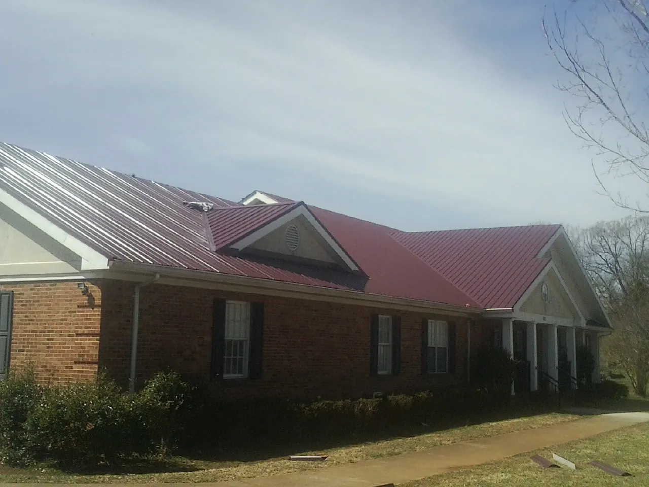 Red metal roof with gabled entries on a long brick building, from a Hail Damage Roof Repair job in Mattoon