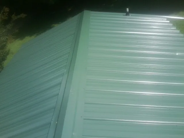 New green metal panels meeting at the ridge of a roof — Flat Roof Repair work by our crew in Mattoon