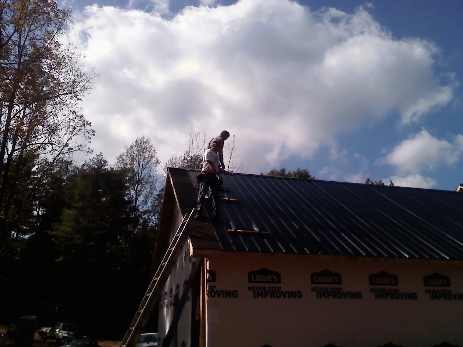 Roofer fastening dark metal panels high against a cloudy sky, from a Roof Inspection job in Mattoon